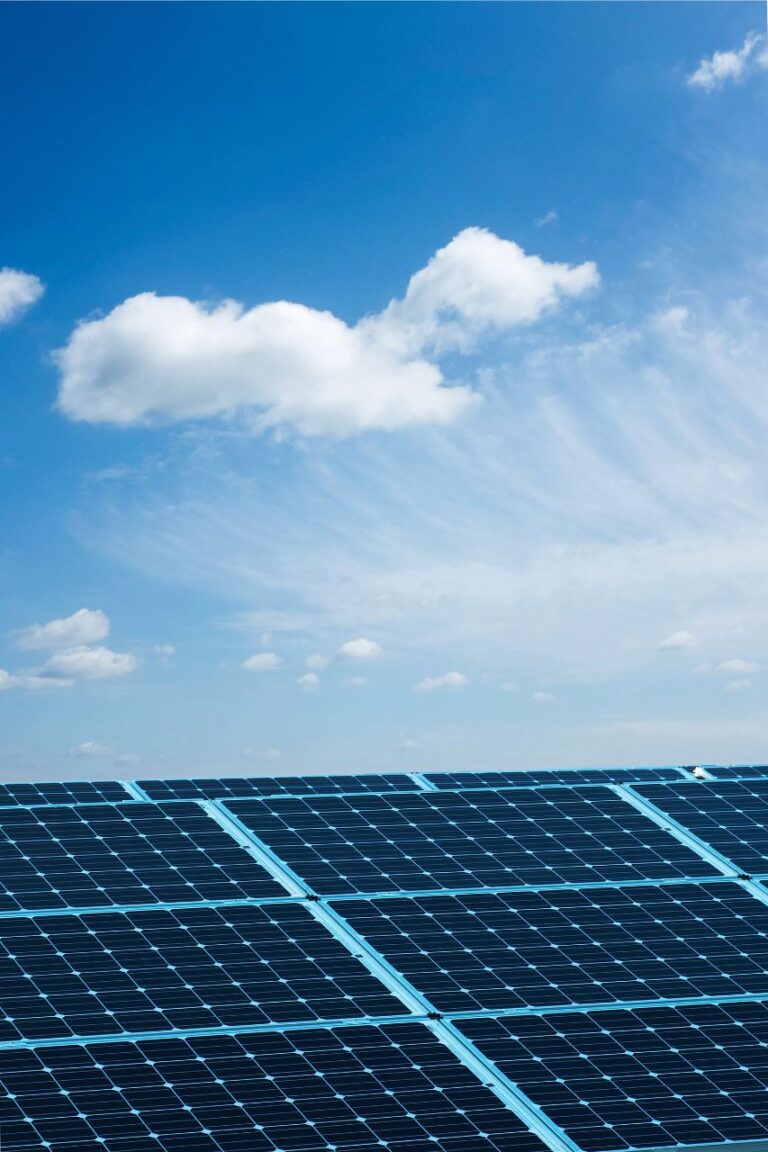 Campo di pannelli fotovoltaici sotto un cielo azzurro con nuvole